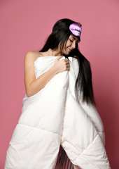 Beautiful brunette girl just woke up with soft blanket and sleepy mask bandage for sleep on pink