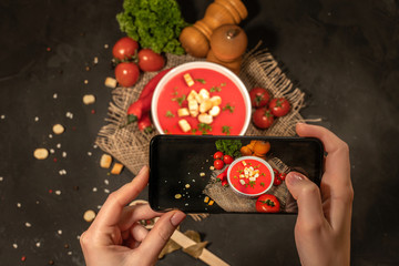 Hands taking photo a delicious tomato soup in a ceramic bowl with smartphone