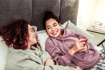 Girlfriends feeling relaxed while lying in bed and having conversation