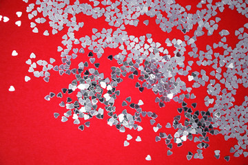 Valentine's Day. Lovers. Textures of silver sequins (paillettes) on a red background. Top view. Small hearts with a reflecting and mirrored surface, producing lights, glows, reflections, glitter