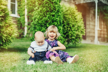 Naklejka na ściany i meble Summer happy time. Two cheerful infant babies outdoors smiling and playing together in green sunny park. Childhood, happiness, infant baby concept