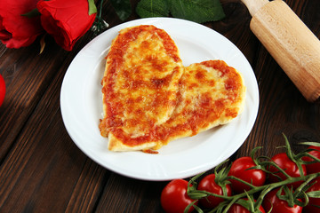 Valentines day pizza in heart shape on dark rustic wooden background.