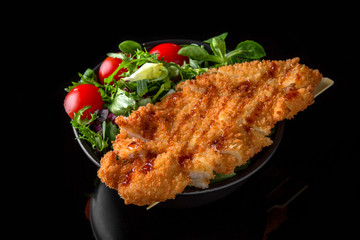 Nutritious dietary salad with chicken, turkey meat and green mix: arugula, valerian, lettuce, Chinese cabbage and tomatoes on black background