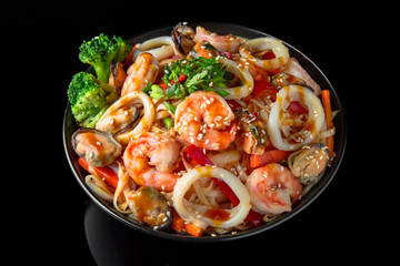 Soba, udon, asian wheat noodles with seafood: shrimps, mussels, squid and vegetables: broccoli, carrots, sweet peppers, zucchini on a black background. Asian style. Japanese food