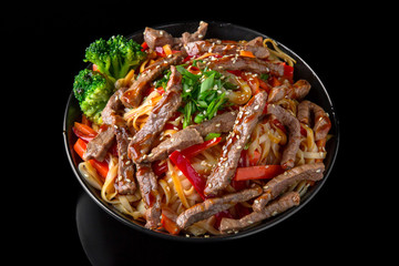 Soba, udon, asian wheat noodles with beef and vegetables: broccoli, carrots, sweet peppers, zucchini on a black background. Asian style. Japanese food