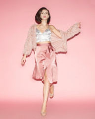 young fashion woman in pink clothes run on pink background; full lenght; front view