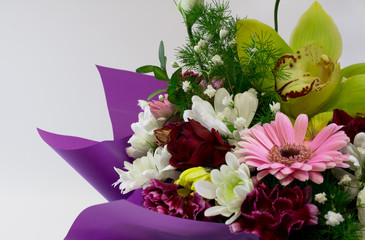 View of a part of a large bouquet of multicolored flowers, which is decorated with green grass with different spring flowers and a purple  wrap