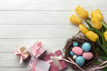 Easter background with blue and pink eggs in nest, gifts and yellow tulips. Top view with copy space.
