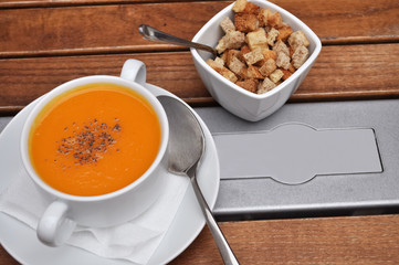 Yellow pumpkin soup puree and bread rusks in white plates on a wooden table.