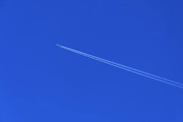 Flight of the plane with a white trace diagonally against a clear blue sky