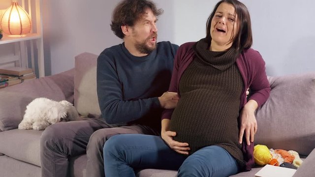 Pregnant woman at home starting to feel contractions sitting on sofa husband getting worried