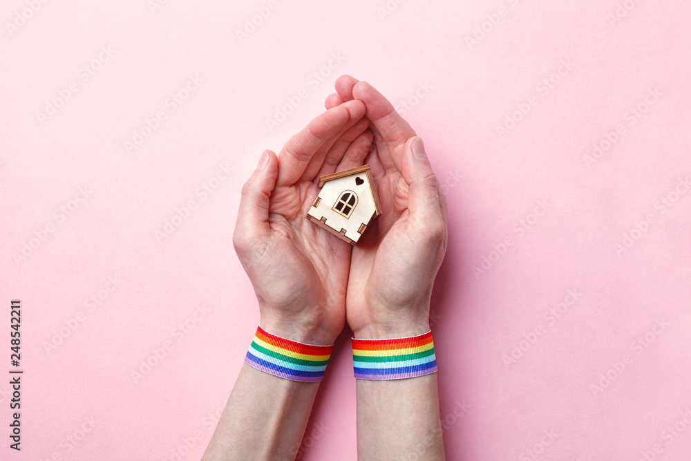 Wall mural female hand with rainbow gay pride lgbt ribbon wristband holding small wooden house