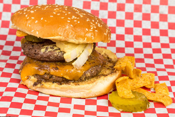 Large Cheeseburger with Pickles and Onions on Red Plaid Wrapper with Chips