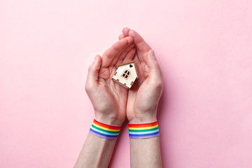 female hand with rainbow gay pride LGBT ribbon wristband holding small wooden house