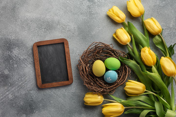 Easter background with blue and pink eggs in nest and yellow tulips. Top view with space for your greetings