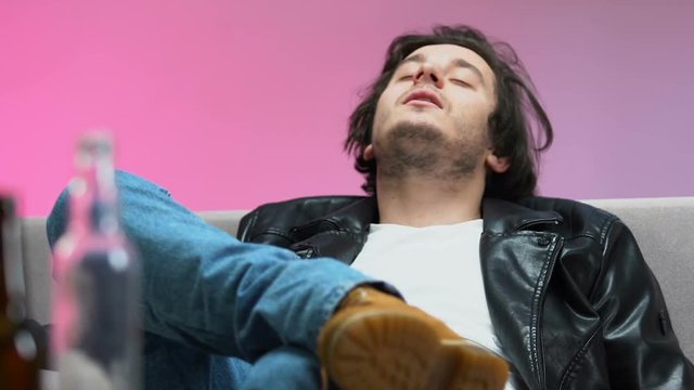 Young drunk man lying on couch, feeling rhythm of music, home party, idle life