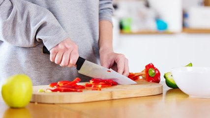 Female cut with a knife pepper at kitchen