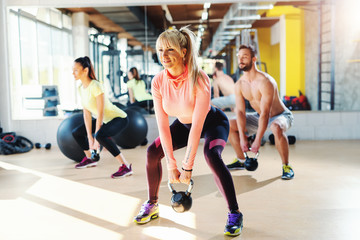 Small group of people with healthy habits swinging kettlebell. Gym interior, mirror in background.male