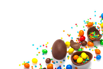 Broken and whole chocolate Easter eggs, multicolored sweets on white background. Concept of celebrating Easter, Easter decorations, search for sweets for Easter Bunny. Flat lay, top view. Copy Space