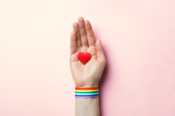 female hand with rainbow LGBT ribbon wristband holding red heart