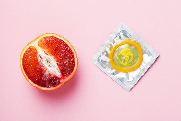 fresh grapefruit and yellow condom on pink background
