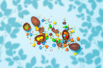 Fototapeta na wymiar Broken and whole chocolate Easter eggs, multicolored sweets on blue background. Concept of celebrating Easter, Easter decorations, search for sweets for Easter Bunny. Flat lay, top view. Copy Space