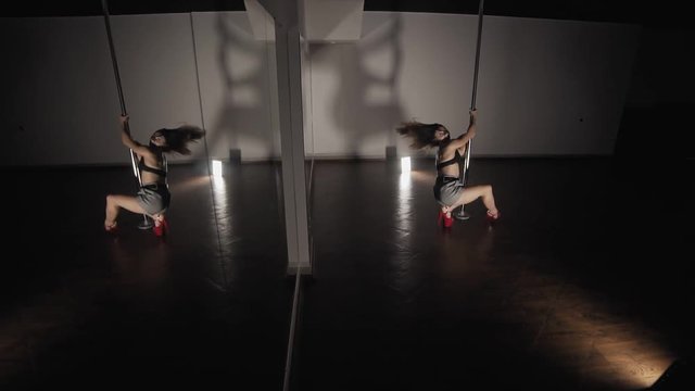 Woman pole dancing at dark studio with mirror. Woman with sexy shape is dancing near the pole in slow motion. Dancer moving with pylone