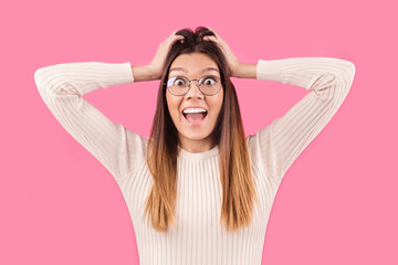 Fototapeta premium Beautiful woman stares at camera with big eyes, wears spectacles, isolated over pink background. Pretty girl sees shocking situation