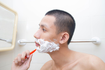Young man shaving in bathroom