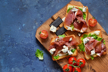 Naklejka na ściany i meble Bruschetta with prosciutto, salad frieze and cheese on the kitchen table. Snack. View from above.