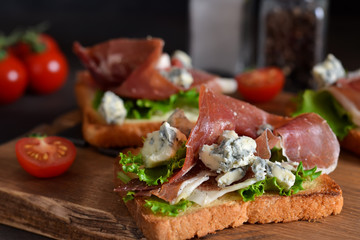 Bruschetta with prosciutto, salad frieze and cheese on the kitchen table. Snack.