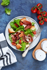 Salad with prosciutto, cherry tomatoes, bread crisps on the kitchen table. View from above.