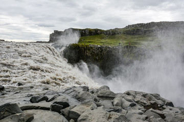 Fresh clean Dettifoss waterfall  in Iceland in  summer with loads of water flowing and mist, rocks in foreground