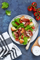 Salad with prosciutto, cherry tomatoes, bread crisps on the kitchen table. View from above.