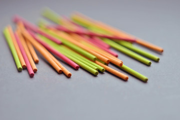 Multi-colored short Indian incense sticks lie on a dark gray background closeup, with copyspace
