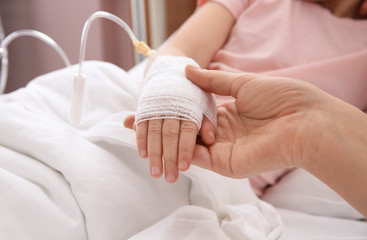 Doctor holding little child's hand with intravenous drip in hospital, closeup