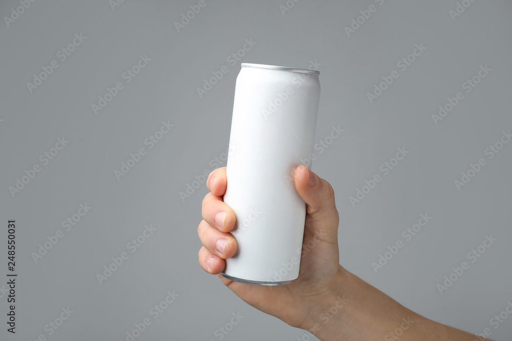 Poster Man holding aluminum can with beverage on grey background, closeup. Space for design