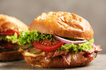 Delicious burger with bacon on table against grey background