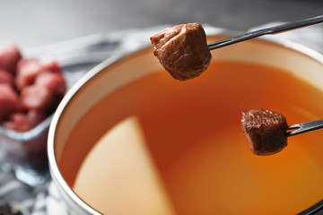 Dipping meat into fondue pot with oil on table, closeup