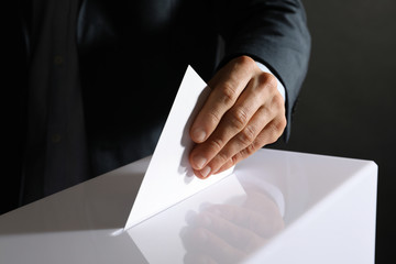Man putting his vote into ballot box on black background, closeup