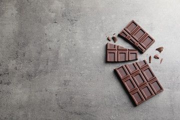 Pieces of tasty chocolate on grey background, flat lay. Space for text
