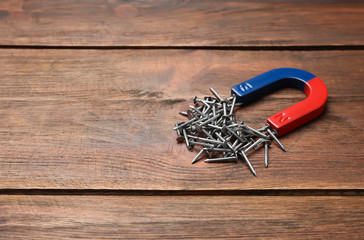 Magnet attracting nails on wooden background, space for text