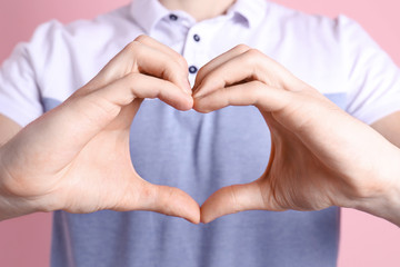 Young man making heart with his hands on color background, closeup