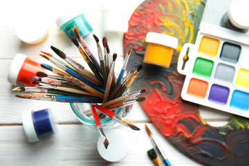 Glass jar with brushes, paints and palette on wooden background, top view