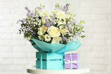 Beautiful bouquet of flowers in decorative crate and gift box on table against light background