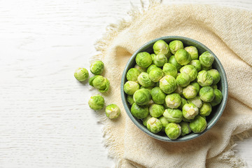 Bowl of fresh Brussels sprouts and napkin on wooden background, top view with space for text