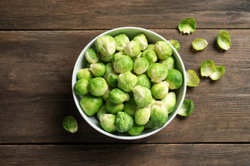 Bowl of fresh Brussels sprouts and leaves on wooden background, top view