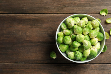 Bowl of fresh Brussels sprouts and leaves on wooden background, top view with space for text