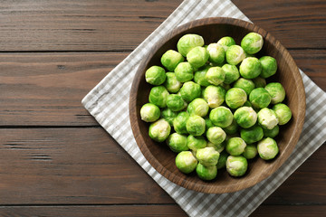 Bowl of fresh Brussels sprouts and napkin on wooden background, top view with space for text