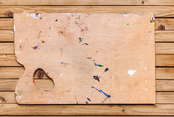 A wooden palette of the artist lies on a brown rustic table.